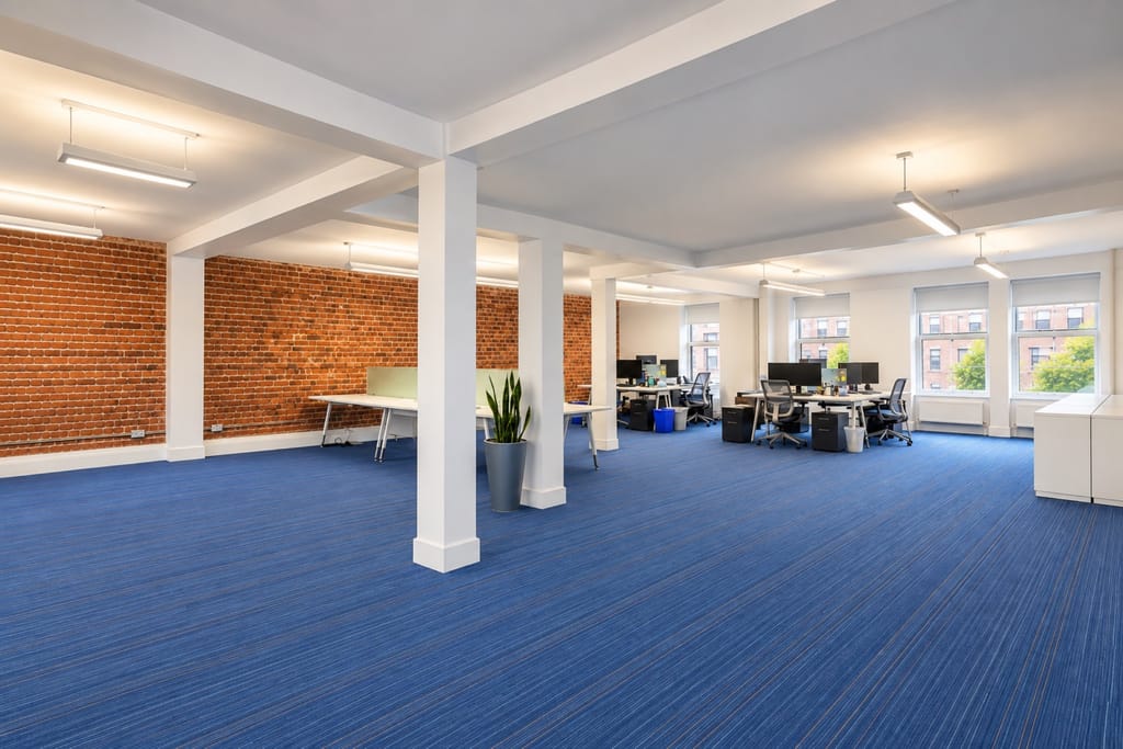 Les bureaux loués d'Adviso : brique, moquette bleue et postes de travail.